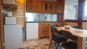 A compact kitchen with wooden cabinets, a white refrigerator, a dishwasher, and a dining table with chairs.