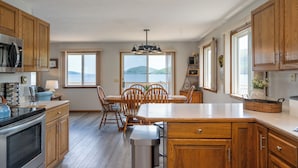 A kitchen with wooden cabinets, a stainless steel microwave, and a dining area with a table and chairs. - The Chosen Spot: Secluded, Views, Wineries, Hot tub, Skiing, Pet friendly! (Naples)