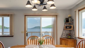 A dining area with a table set for four, a vase with flowers, candles, and a view of the sea through large windows. - The Chosen Spot: Secluded, Views, Wineries, Hot tub, Skiing, Pet friendly! (Naples)