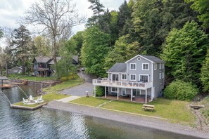 A large house with a deck and a dock by a lake, surrounded by trees.