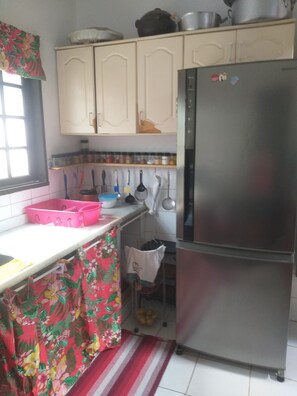 Uma cozinha com armários brancos, uma geladeira de aço inoxidável e diversos utensílios de cozinha pendurados na parede.