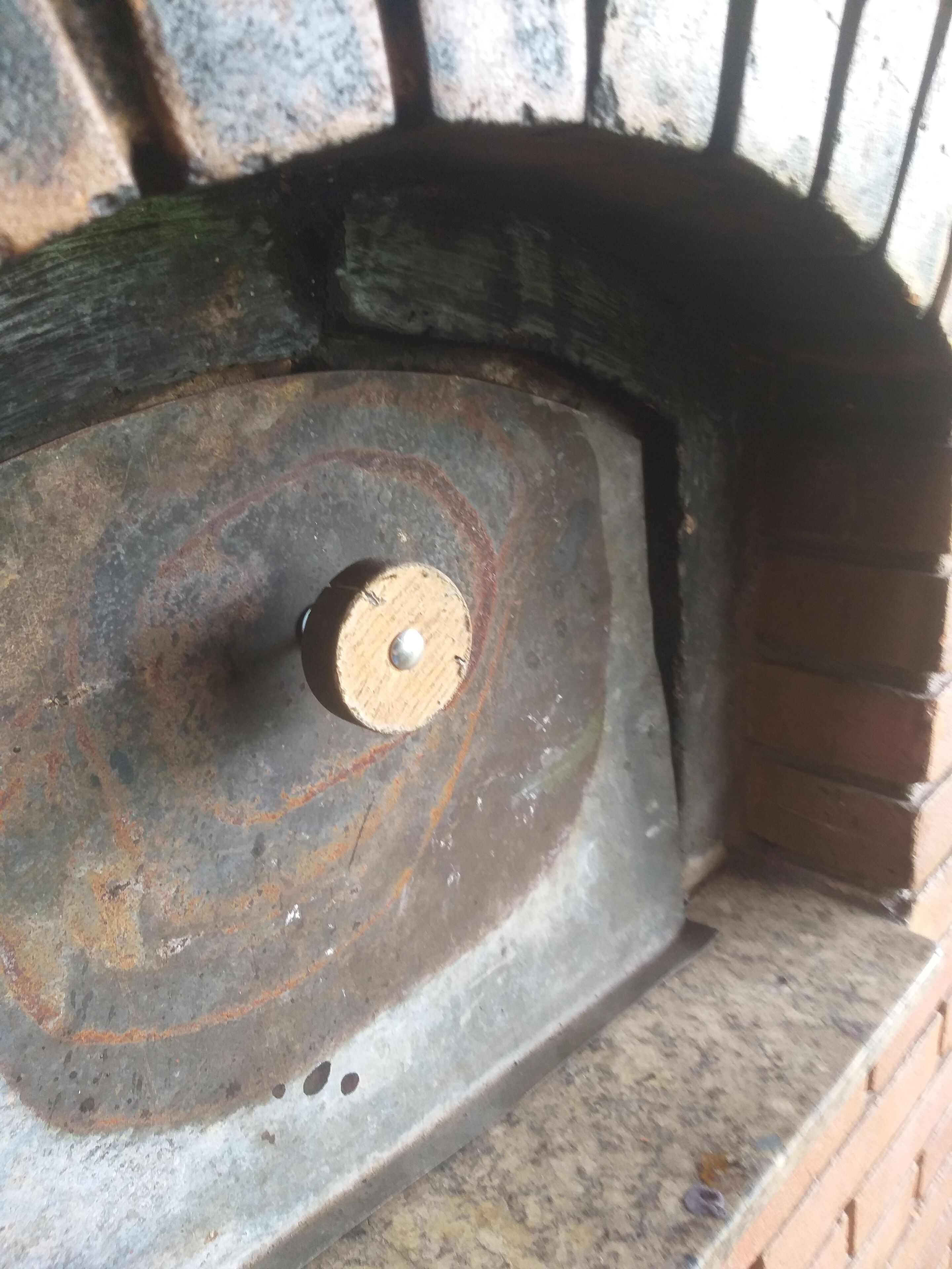 A close-up of a metal surface with a circular pattern and a central bolt, surrounded by a brick structure.