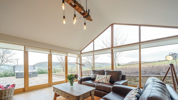 A spacious room with a leather sofa, wooden coffee table, and large windows offering a view of the countryside. - 2 bedroom accommodation in Llantilio Pertholey (Llantilio Pertholey)