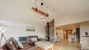 A spacious living area with a leather sofa, a coffee table, a stone fireplace, and a dining area with a table and chairs. - 2 bedroom accommodation in Llantilio Pertholey (Llantilio Pertholey)