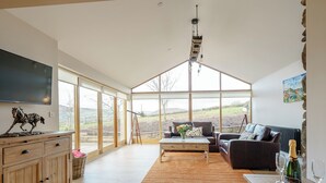 A spacious living room with a large window, a wooden cabinet, a leather sofa, a coffee table, and a telescope. - 2 bedroom accommodation in Llantilio Pertholey (Llantilio Pertholey)
