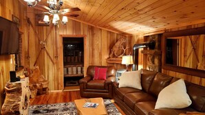L'intérieur chaleureux d'un chalet avec un canapé en cuir marron, une table basse en bois, un tapis à motifs et un ventilateur de plafond.
