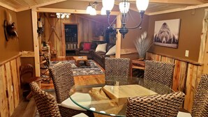 Un intérieur chaleureux avec des éléments en bois, une table à manger au plateau de verre entourée de chaises en osier, un canapé en cuir et un lustre.
