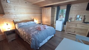 Un dormitorio acogedor de cabaña de madera con cama, mesitas de noche, cómoda y un refrigerador pequeño.