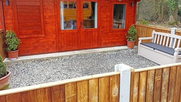 Una cabaña de madera con un patio de grava, una banca y dos macetas.