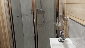 Una ducha con paredes de vidrio, un grifo de cromo y un lavamanos blanco con un grifo de cromo.
