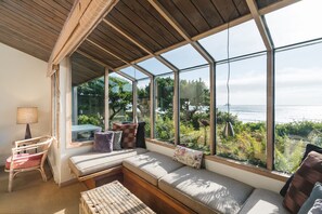 A sunlit room with a large window overlooking a garden and the sea. - Arch Cape Escape by AvantStay | Sensational Clift Top Home w/Pacific Ocean Views (Arch Cape)