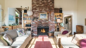 Ein gemütliches Wohnzimmer mit Kamin aus Backstein, bequemen Sitzmöglichkeiten und einem Bücherregal voller Bücher und Dekoration.