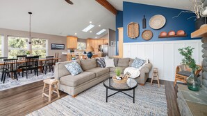 Een ruime woonkamer met een grote hoekbank, een eethoek met houten stoelen en een keuken op de achtergrond.