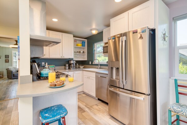 Una cocina moderna con armarios blancos, un refrigerador de acero inoxidable y una zona de bar con taburetes.