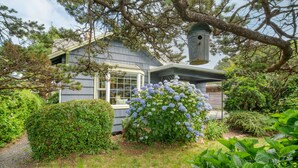 A house with a covered porch, a birdhouse, and a well-maintained garden with hydrangeas.