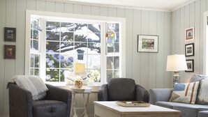A cozy living room with a large window, two armchairs, a coffee table, and a side table with a lamp.