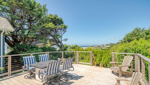 A wooden deck with a table and chairs, surrounded by greenery and overlooking a scenic view.