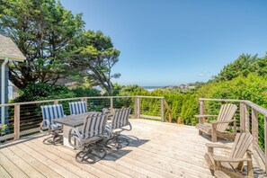 Una terraza de madera con una mesa y sillas, rodeada de follaje y con vistas panorámicas.