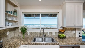 Una cocina con encimera de granito, pileta de acero inoxidable y ventana con vista al océano.