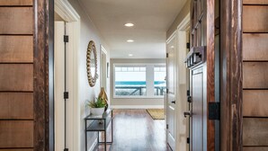 Un pasillo con paneles de madera, una planta en maceta y vista al océano a través de un ventanal grande.