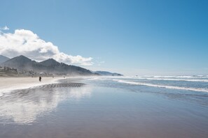 A beach with a mountain in the background and a few people walking along the shore. - Blue Starfish by AvantStay | Ocean Views & Direct Cannon Beach Access (Cannon Beach)