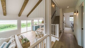 A spacious interior with a high ceiling, wooden beams, a dining area with a table and chairs, and a staircase leading to another level.
