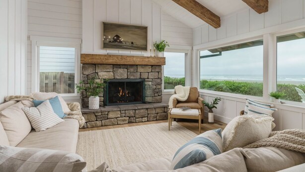 A cozy living room with a stone fireplace, wooden beams, and a view of the ocean.