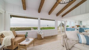 A spacious living area with large windows, a wooden ceiling, and a view of the beach.