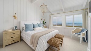 A bedroom with a large bed, a nightstand, a chair, and a view of the ocean.