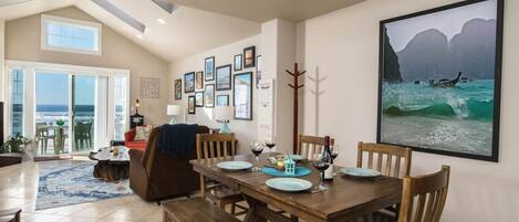 Un comedor con una mesa de madera, sillas y vista al océano a través de amplios ventanales.