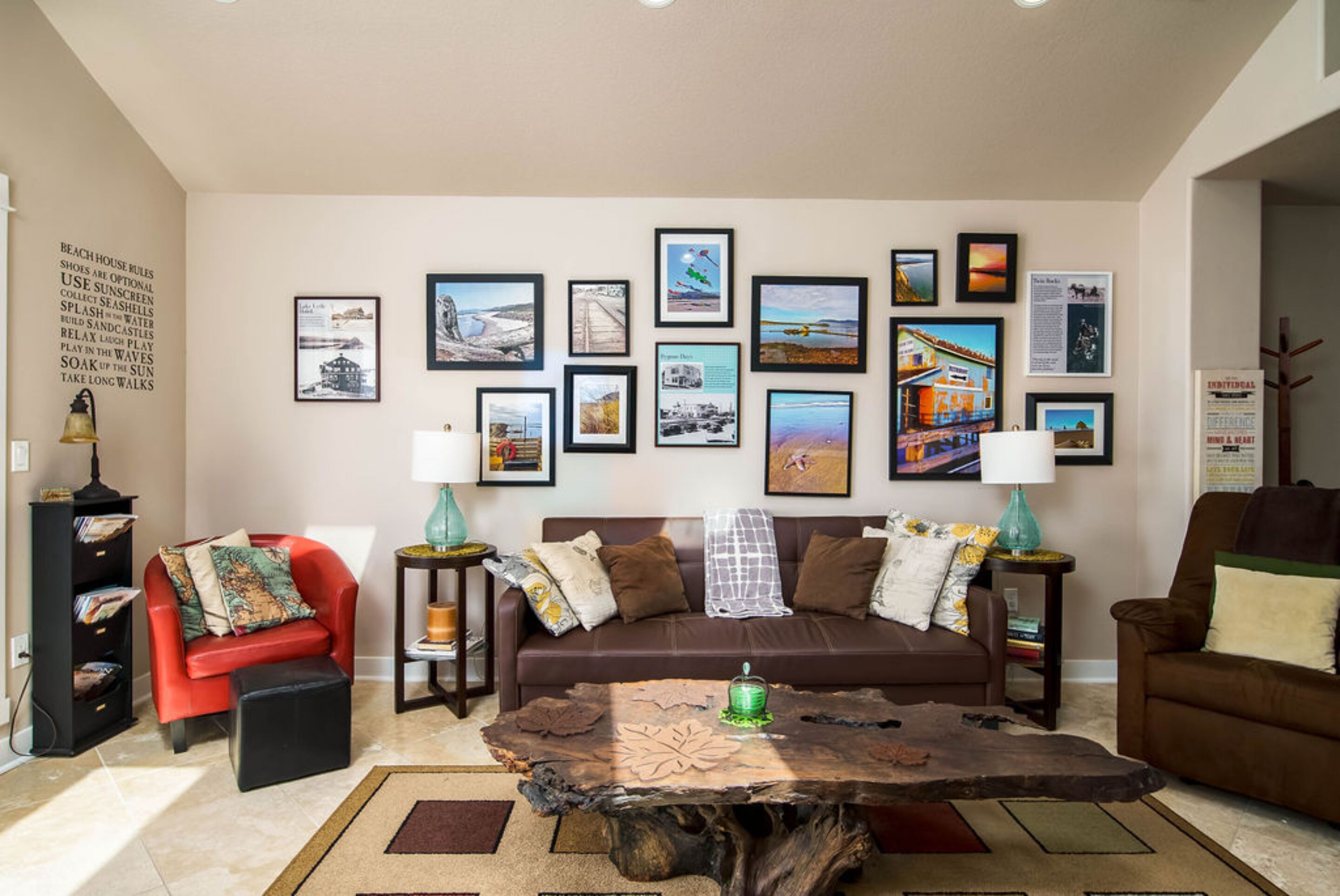 A living room with a brown sofa, a red chair, a coffee table with a tree stump top, and a wall adorned with framed pictures.