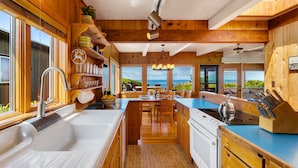 A modern kitchen with wooden cabinetry, a large island, and a view of the ocean. - The Pilot House by AvantStay | Stunning Home Right On Arch Cape Beach! (Arch Cape)