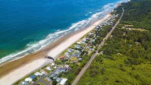 An aerial view of a coastal residential area with a beach, houses, and a road. - The Pilot House by AvantStay | Stunning Home Right On Arch Cape Beach! (Arch Cape)