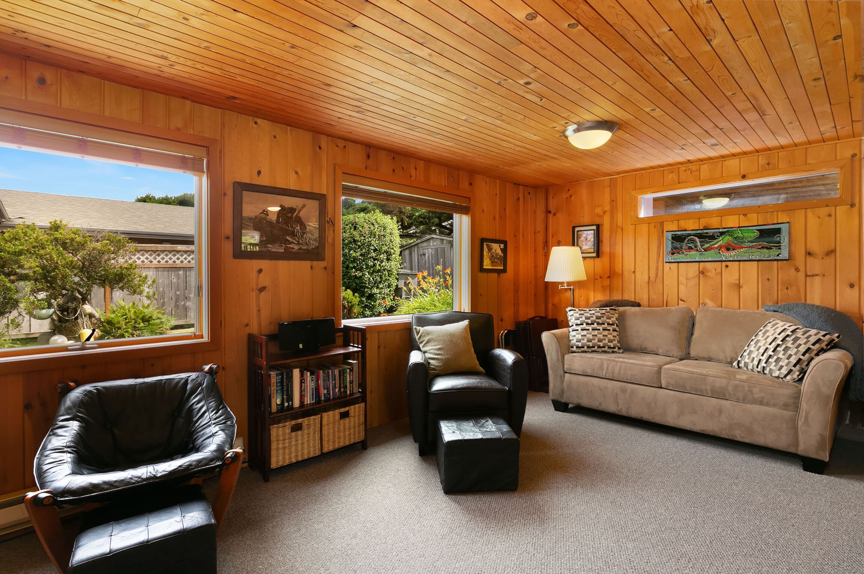 A cozy living room with wooden walls, a leather chair, a sofa, and a bookshelf.