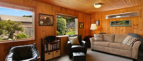 A cozy living room with wooden walls, a leather chair, a sofa, and a bookshelf.