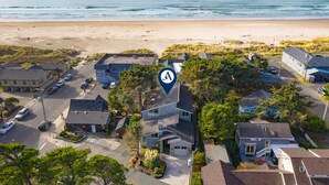 Vue aérienne d’une zone résidentielle côtière, avec des maisons, une plage et un ciel dégagé.