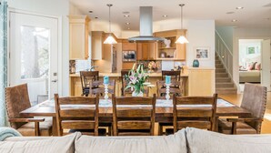 Un grand espace à manger avec une table et des chaises en bois, une cuisine à l’arrière-plan et un escalier menant à un autre niveau.