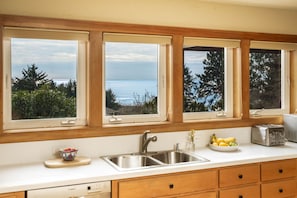 A kitchen with a large window overlooking the sea, a sink, and a toaster.