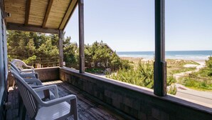 Una terraza de madera con sillas que da a una playa y el océano.