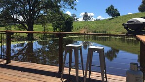 A wooden deck with a view of a pond, a barbecue grill, and a propane tank.