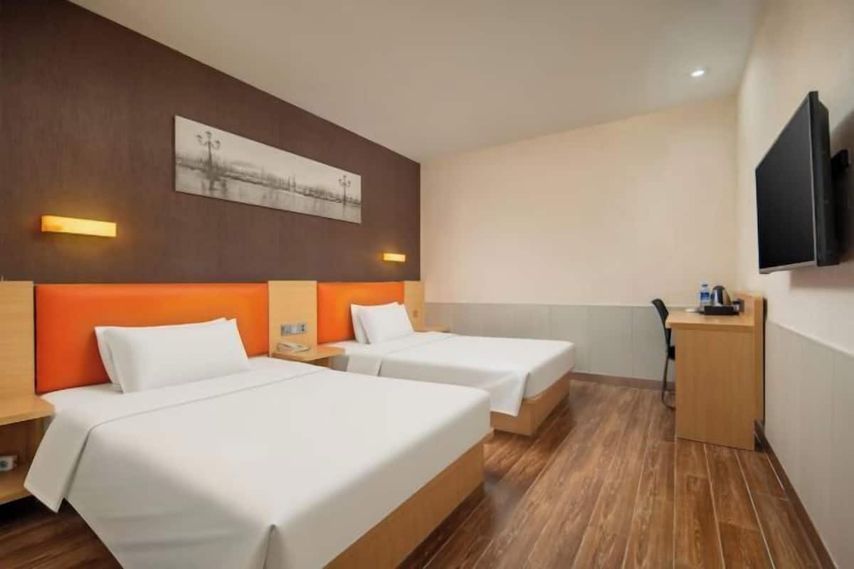 A hotel room with two beds, a desk, a chair, a flat-screen TV, and a painting on the wall.
