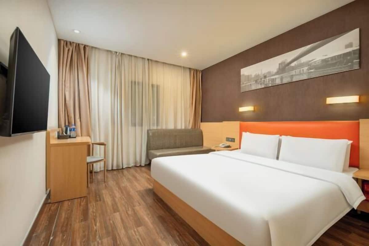 A hotel room with a bed, a desk, a chair, a television, and a painting on the wall.