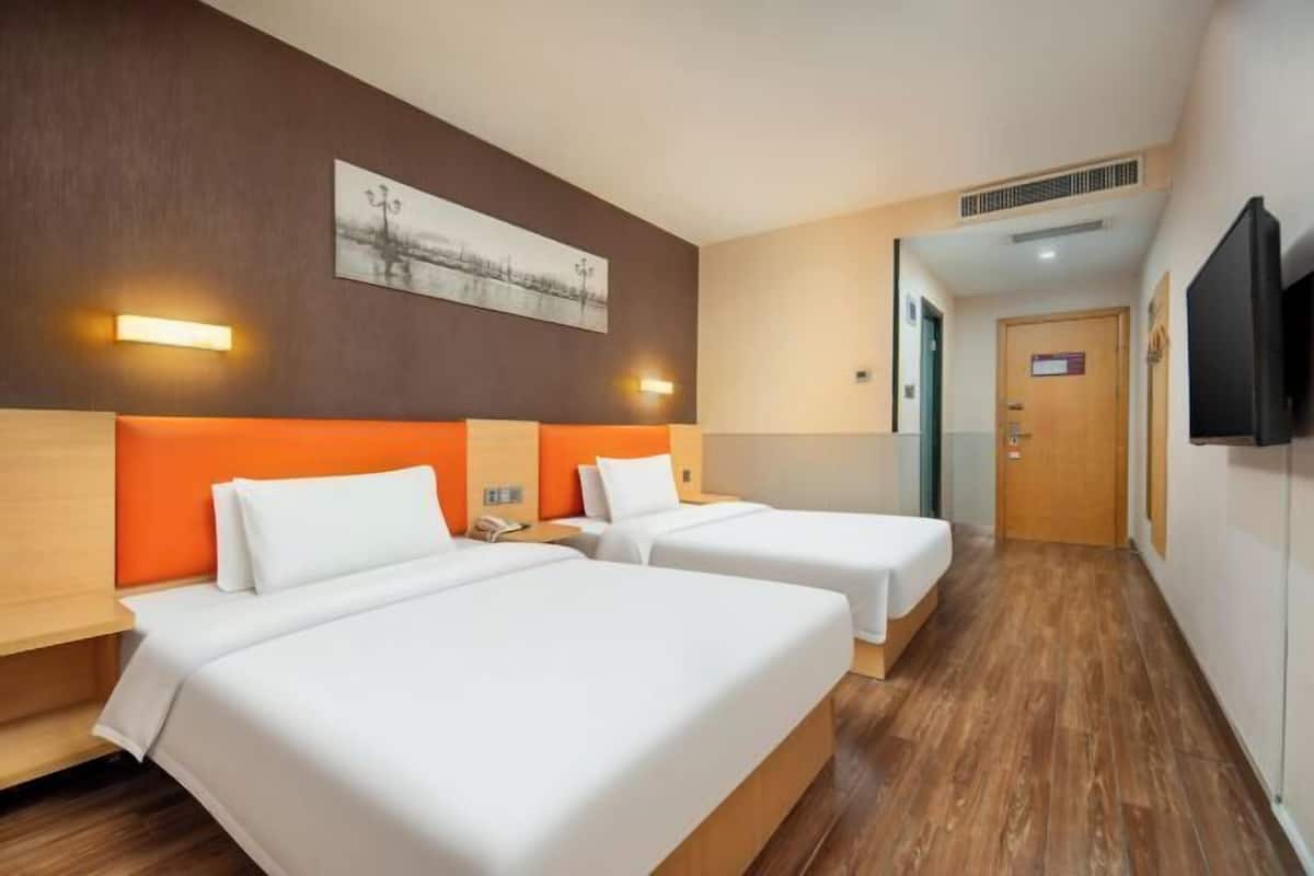 A hotel room with two beds, a painting on the wall, and a television on the wall.