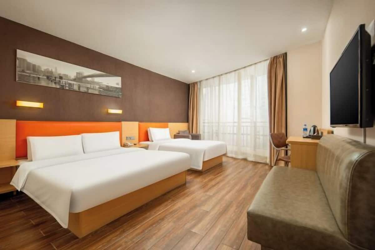 A hotel room with two beds, a sofa, a TV, and a cityscape painting on the wall.