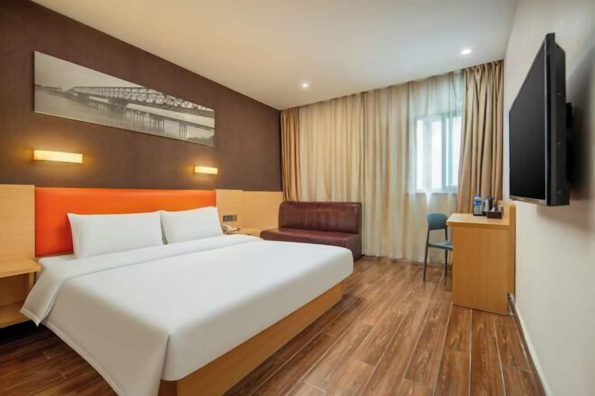 A hotel room with a large bed, a desk, a chair, a TV, and a window with curtains.