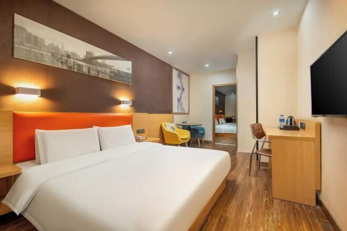 A hotel room with a large bed, a desk, a chair, and a TV mounted on the wall.