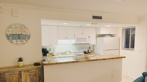 Una cocina moderna con armarios blancos, encimera de granito, microondas integrado y refrigerador.