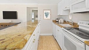 Una cocina moderna con armarios blancos, encimera de granito, estufa integrada y televisor de pantalla plana.