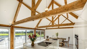 A spacious kitchen with a large island, wooden beams, and a view of the countryside. - Buckley Farm, Barn 1 - UK36588 (Oswestry)