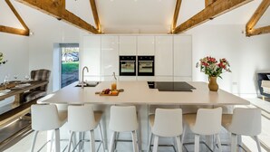 A modern kitchen with white cabinets, a central island with bar stools, and wooden beams on the ceiling. - Buckley Farm, Barn 1 - UK36588 (Oswestry)
